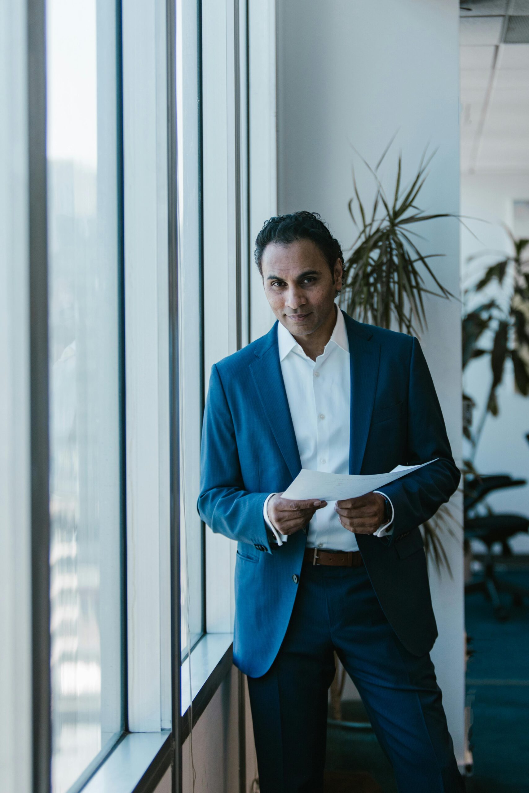 Confident business professional in suit holding documents in a bright office environment.